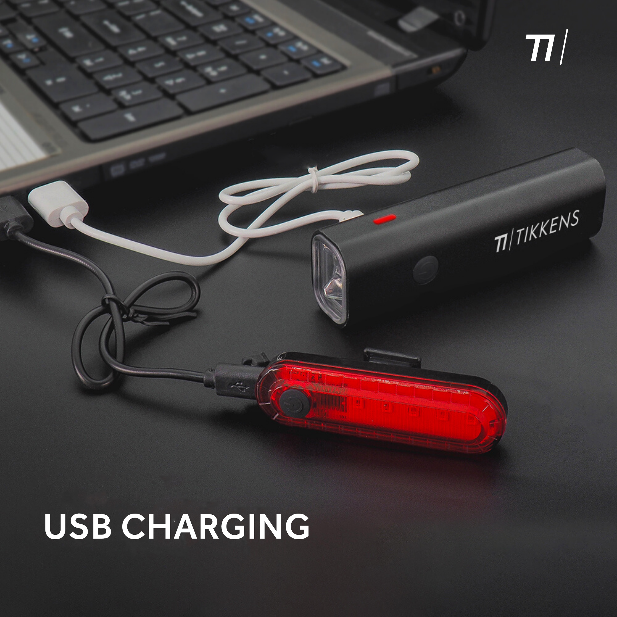 Black bike lights on a black surface. USB charging is written below. A laptop is visible in the background.