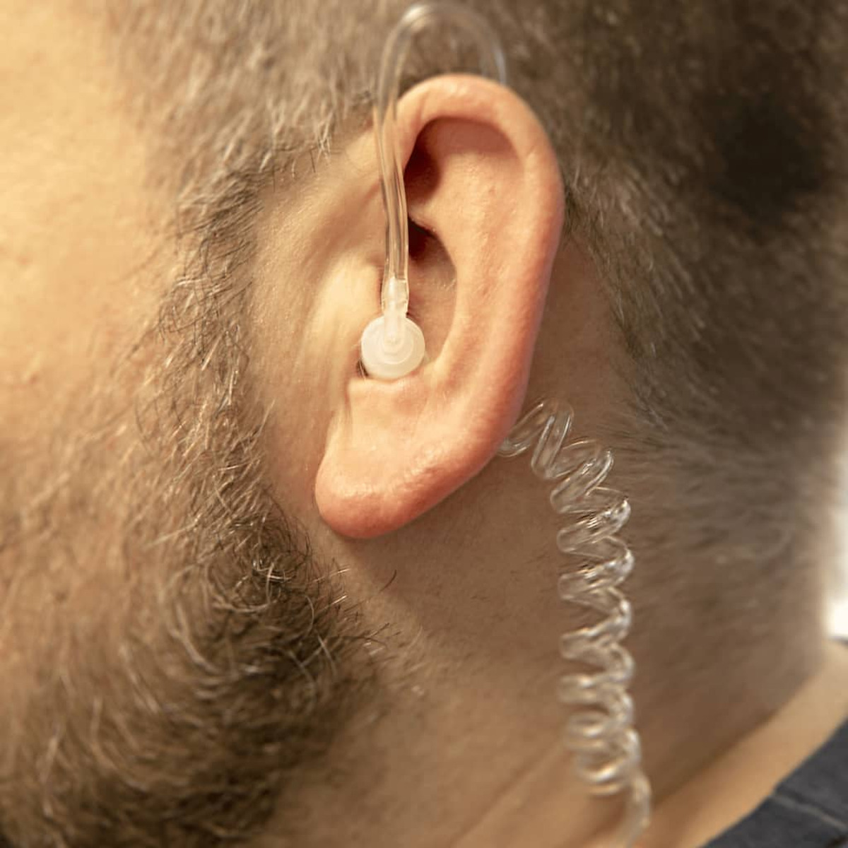Mannes Ohr mit eingesetztem In-Ear-Monitor. Ein spiralförmiger Draht verläuft nach unten.