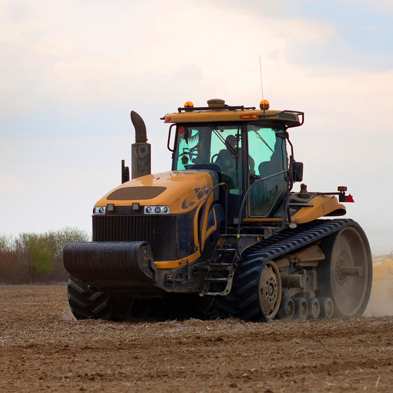 Tractor amarillo en campo. Llantas oscuras, tubo de escape y cabina. Cielo nublado.