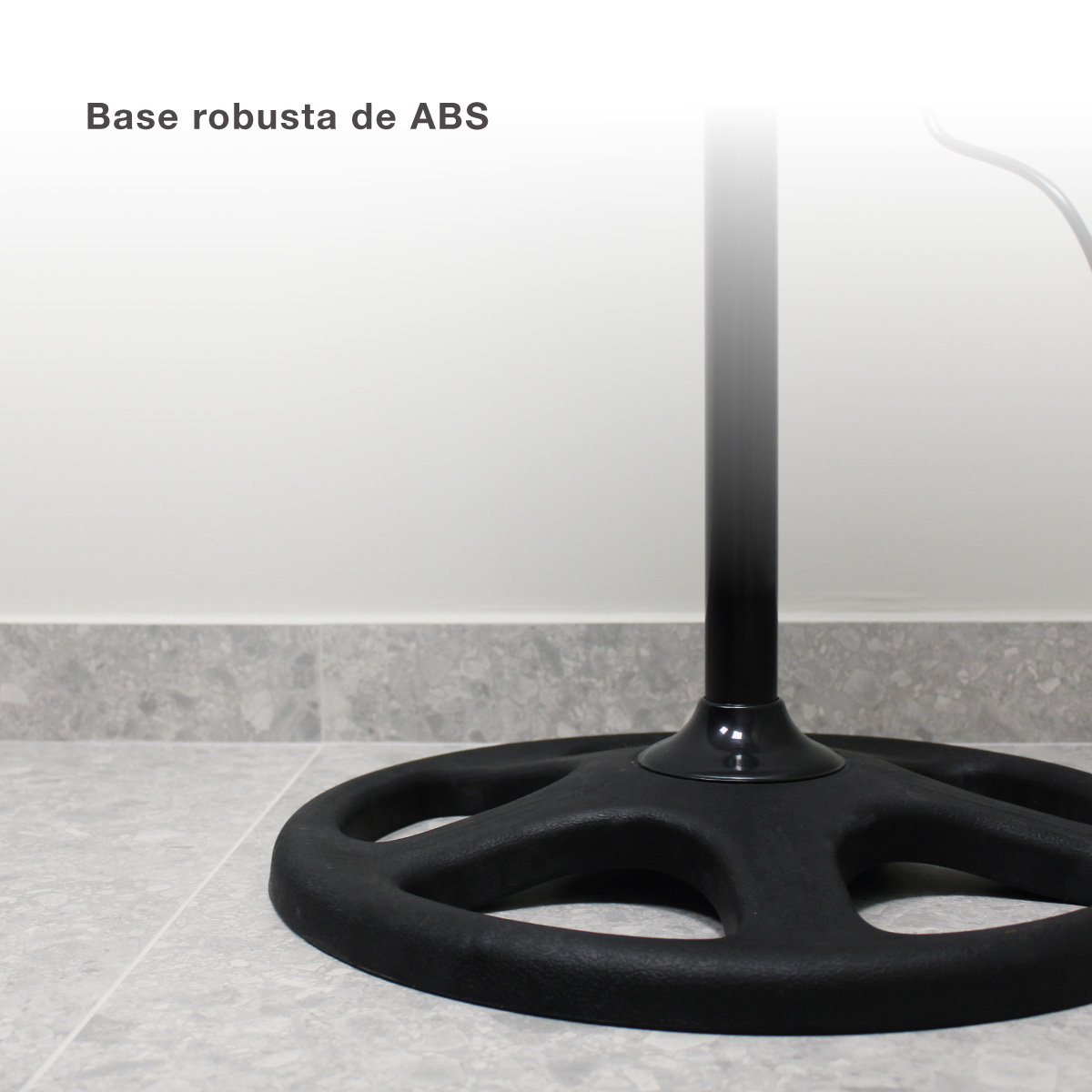 Base de ventilador negra en suelo de baldosas grises. Pared blanca al fondo.