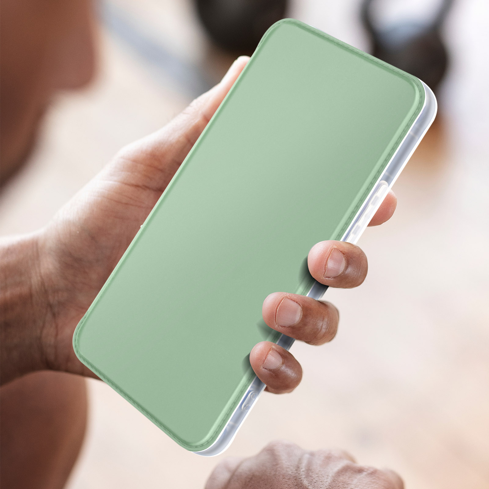Mano che tiene un telefono in una custodia verde, con uno sfondo sfocato che mostra il tono della pelle.