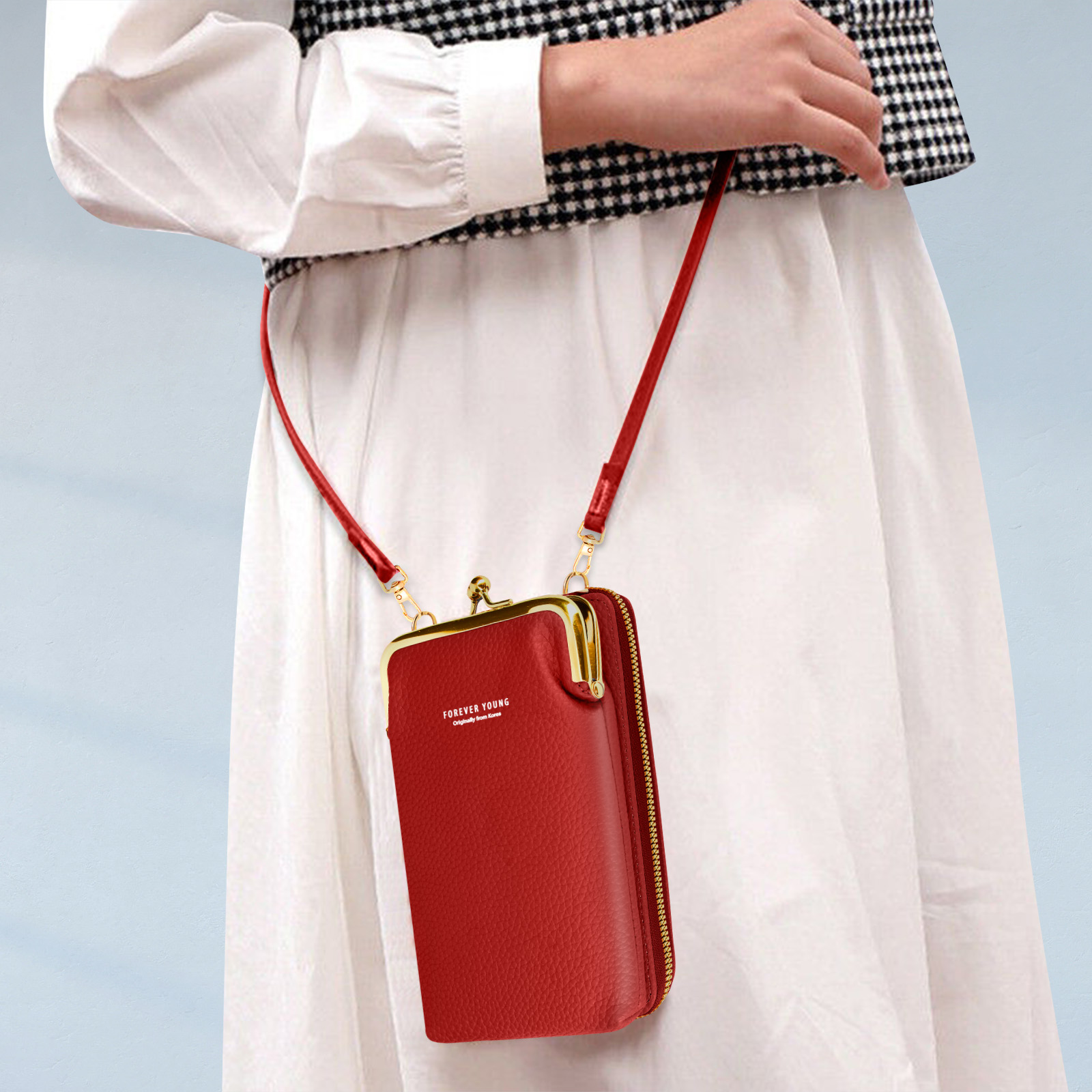 Een persoon die een rode crossbodytas met een gouden sluiting vasthoudt.