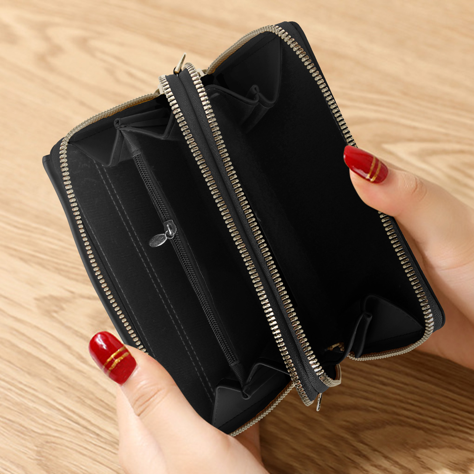 Hände einer Person halten eine offene, schwarze Brieftasche mit mehreren Fächern, mit roten Nägeln.