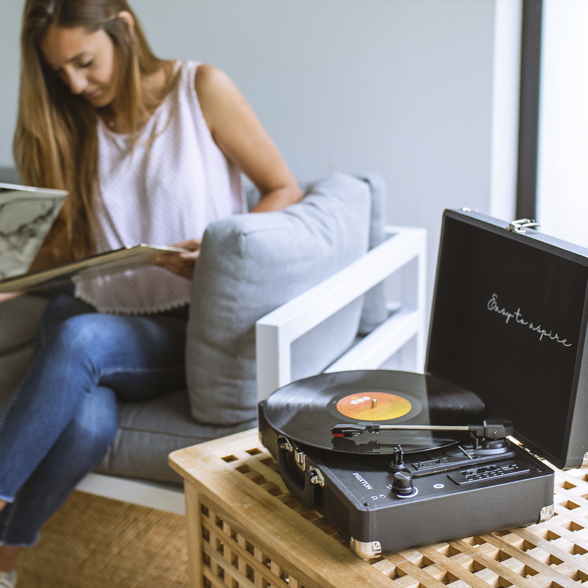 Kobieta słuchająca gramofonu. Płyta na gramofonie, inne płyty na stole.