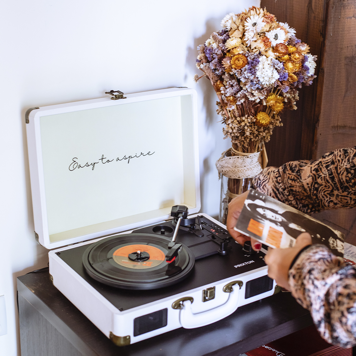 Gramofon z płytą. Kobieta trzyma płytę. Kwiaty w tle.