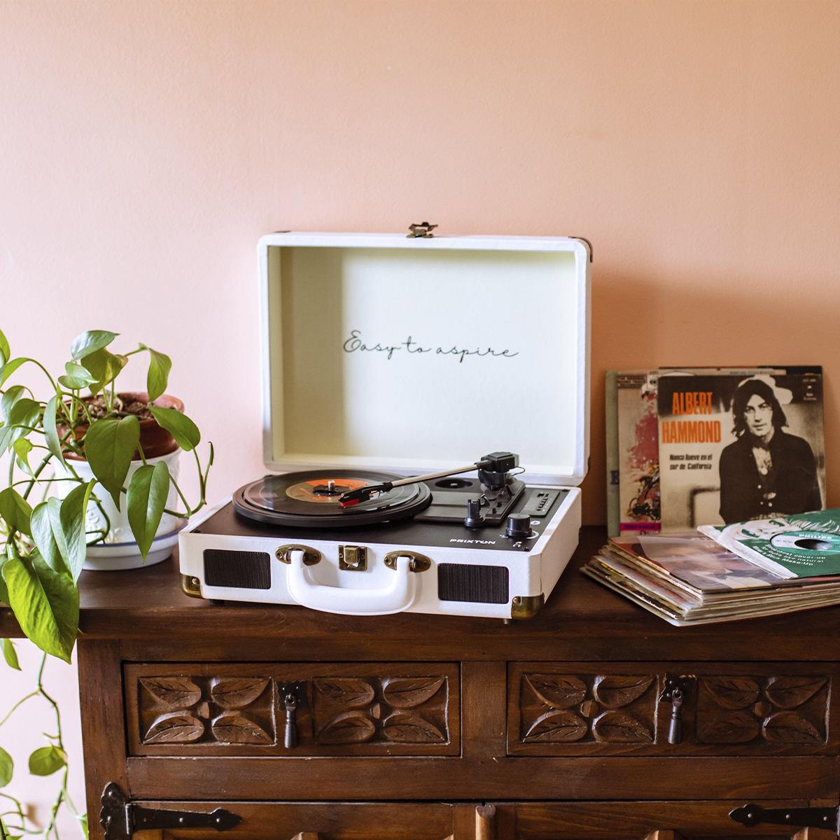 Biały gramofon odtwarza płytę. Płyty winylowe i roślina doniczkowa stoją w pobliżu.