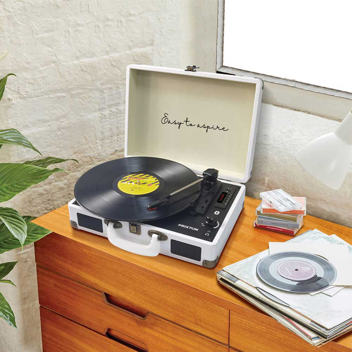 Biały gramofon z płytą. Otwarta walizka i kilka płyt w tle.