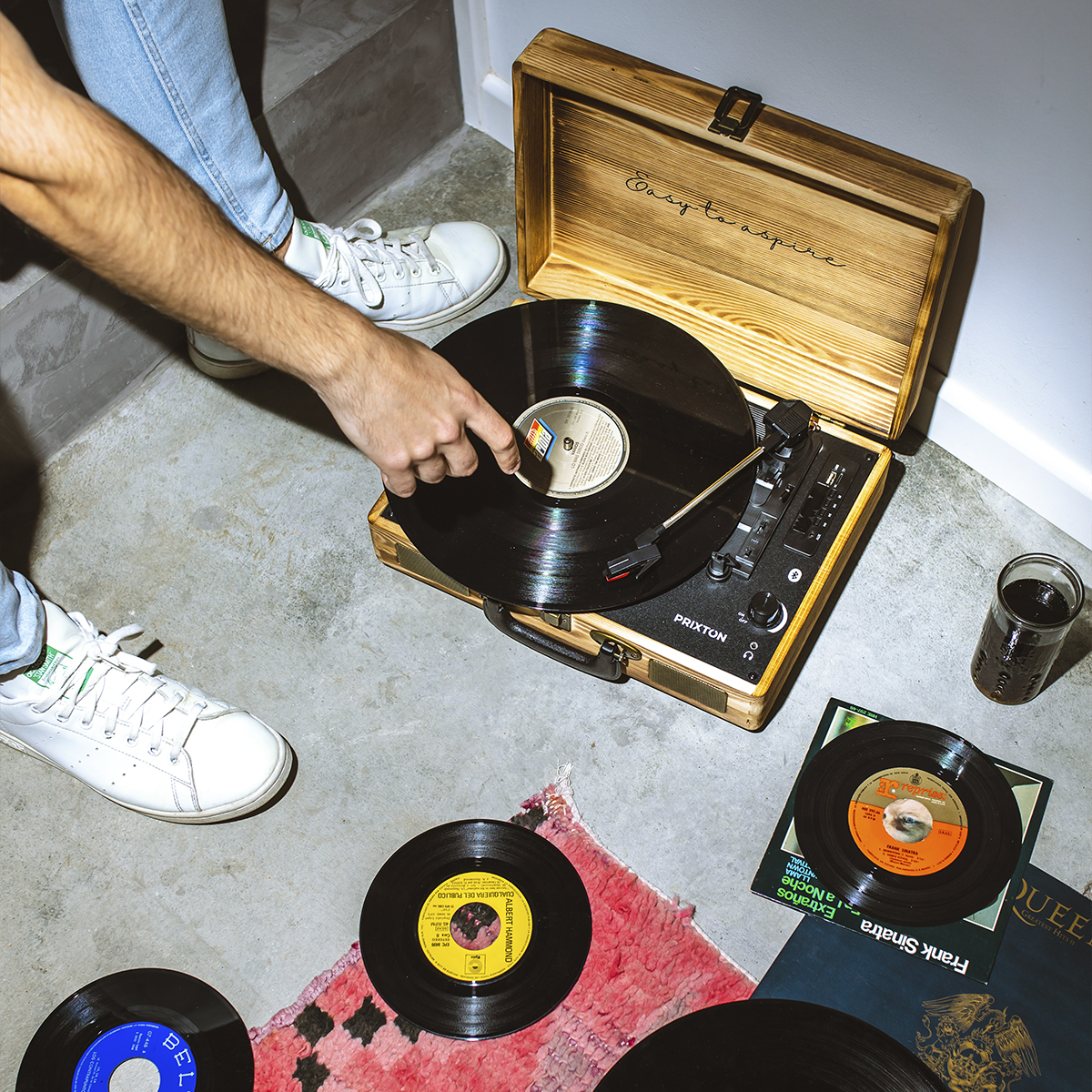 Ręce osoby w pobliżu gramofonu. Płyty winylowe, niektóre w okładkach, na podłodze.