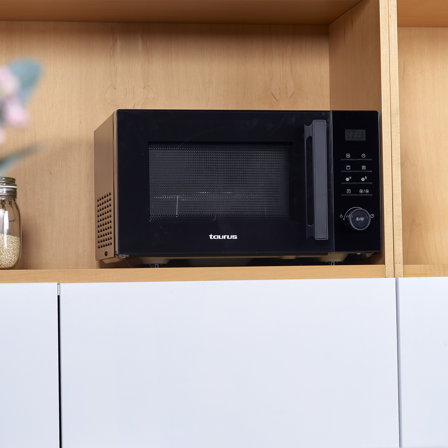 Horno microondas negro en un estante. Se coloca en un mueble blanco. Fondo de madera.