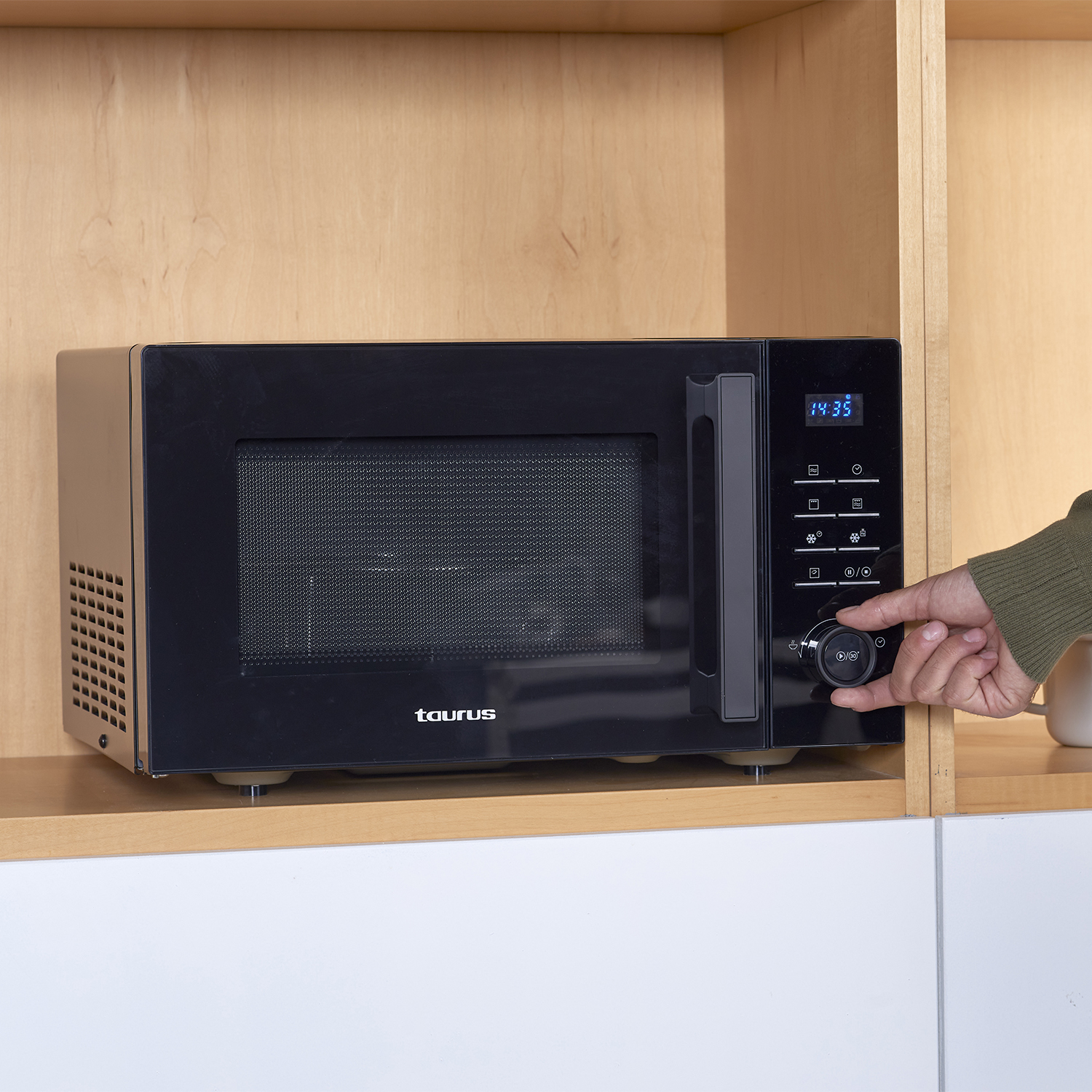 Un horno microondas negro con una pantalla digital, instalado en un gabinete de madera.