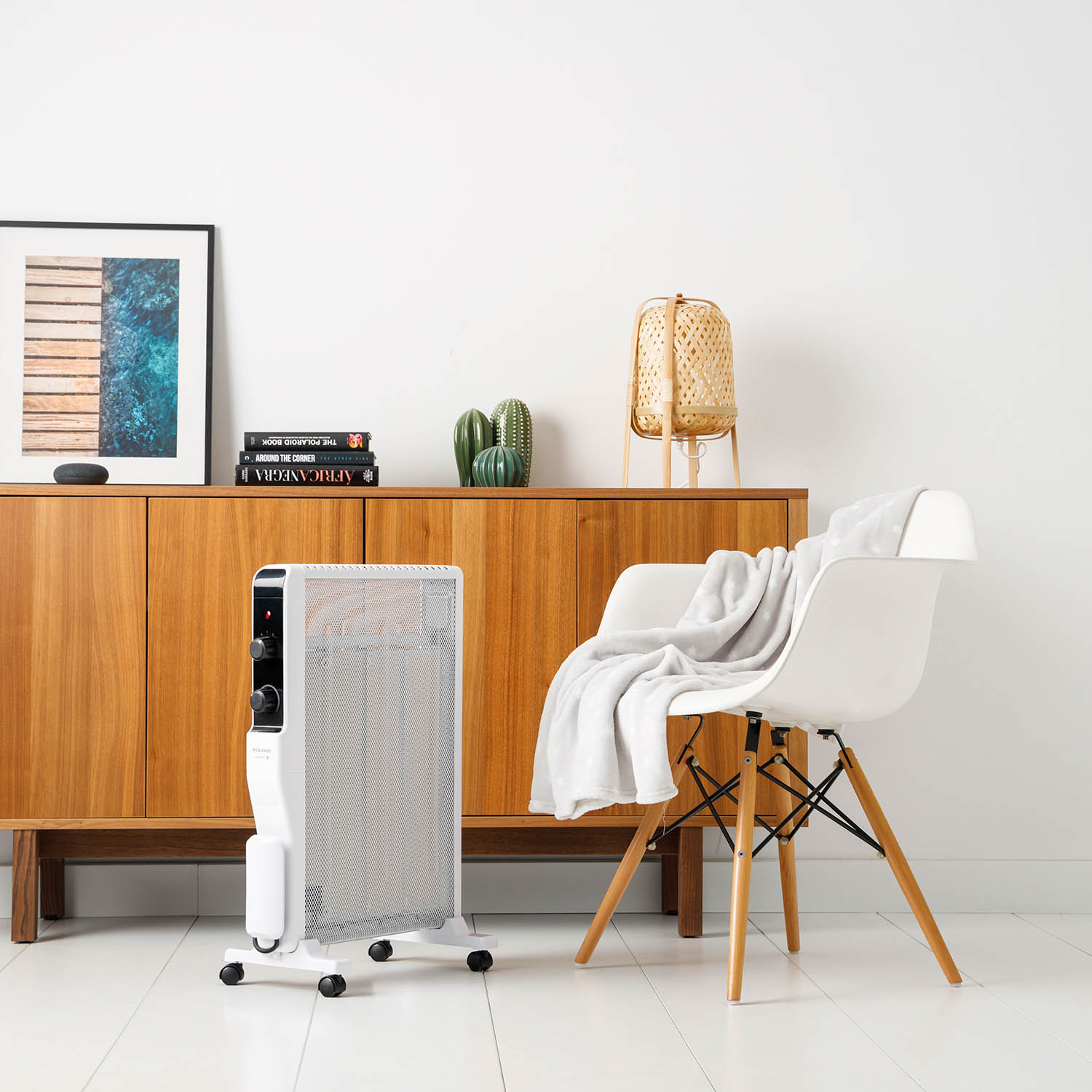 Un calefactor eléctrico blanco, una silla con una manta gris y un mueble con decoración.