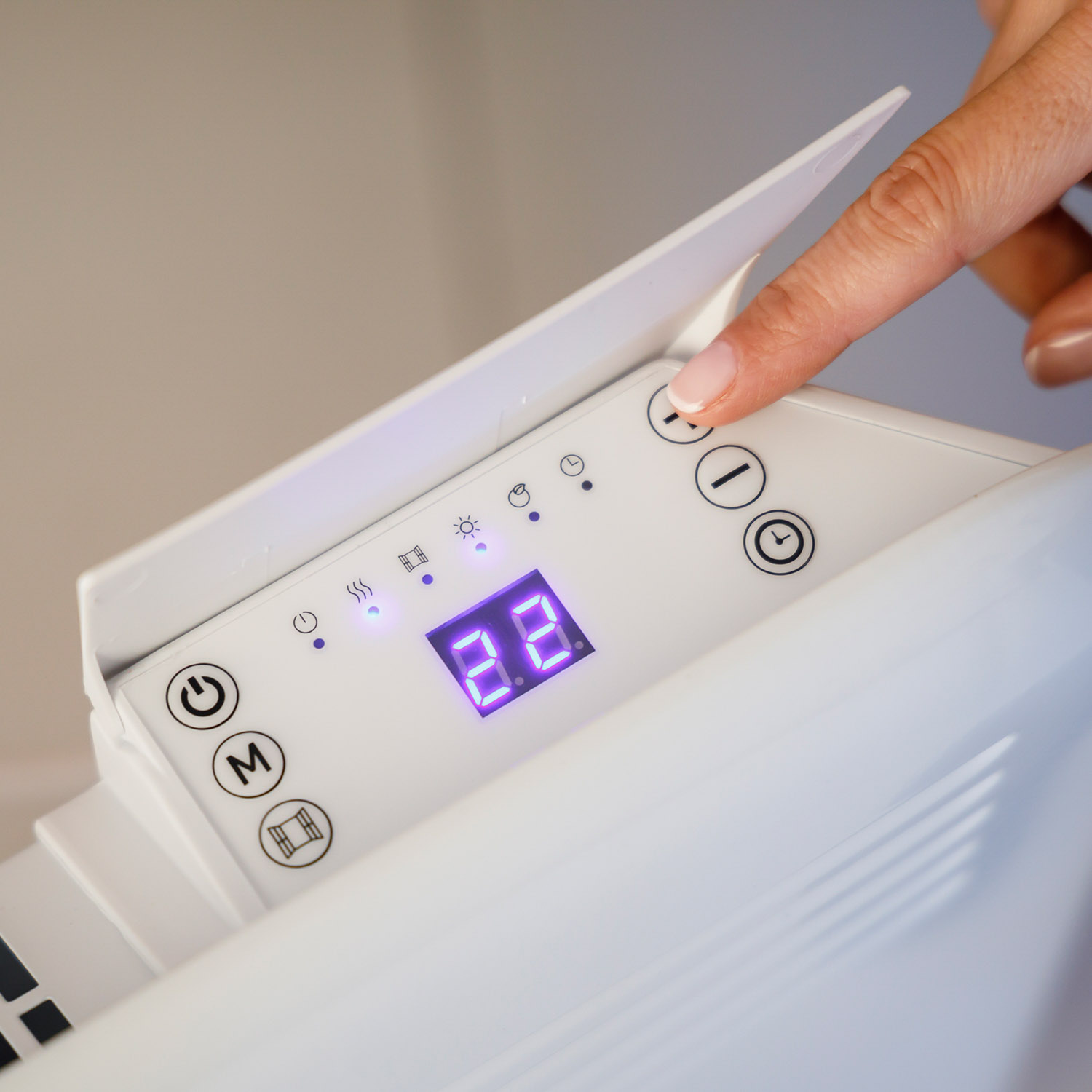 Una mano presiona un botón en un panel de calefactor eléctrico blanco con pantalla digital.