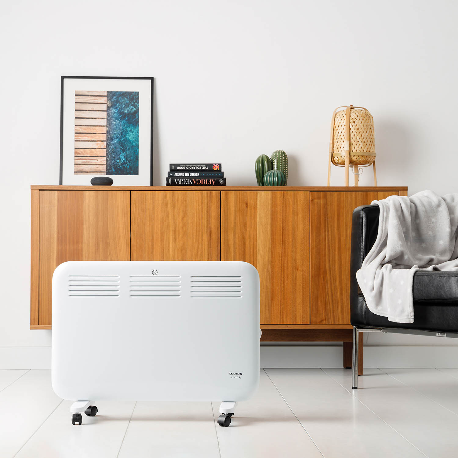 Calentador eléctrico blanco en una habitación. Gabinete de madera y sillón de cuero negro en el fondo. Fondo blanco.