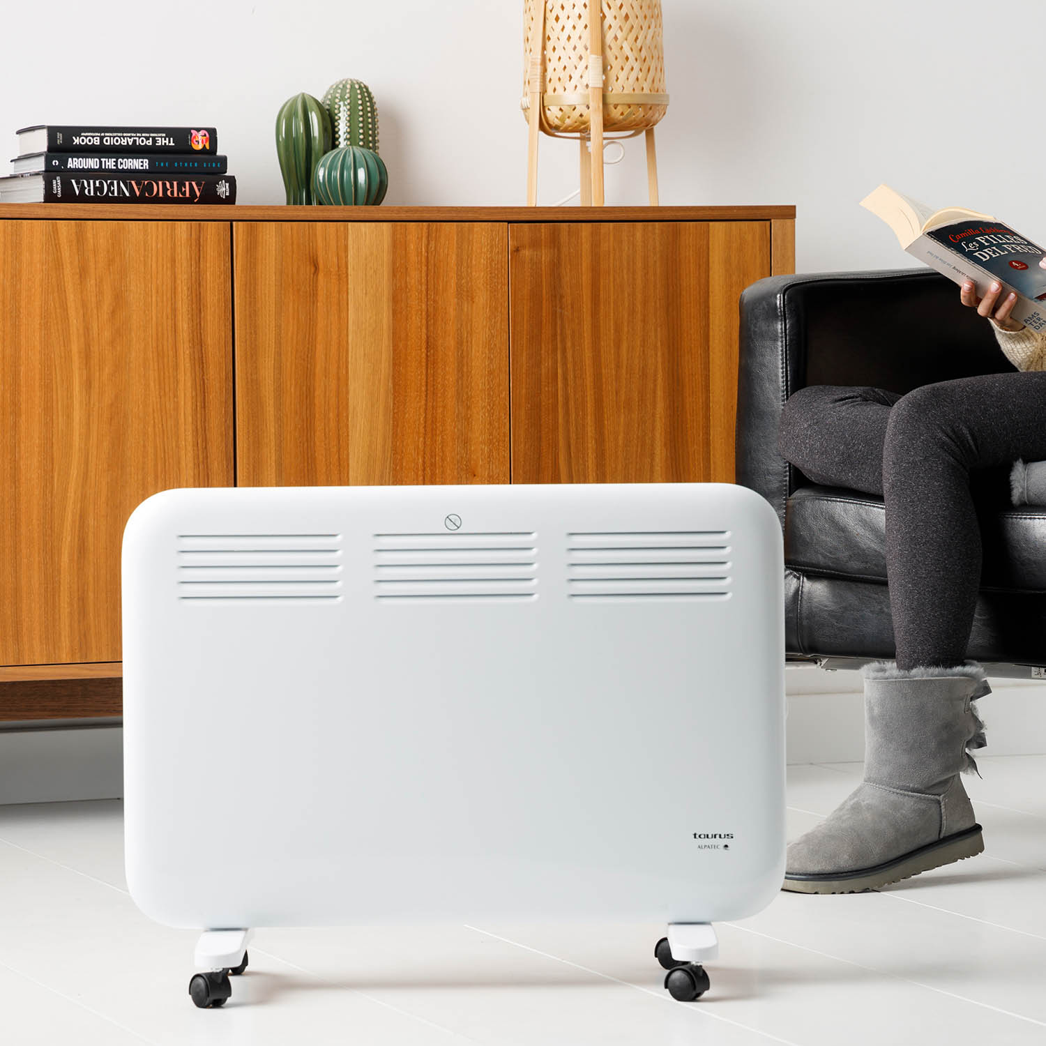 Calentador eléctrico blanco sobre ruedas cerca de una persona leyendo, con libros y decoración.