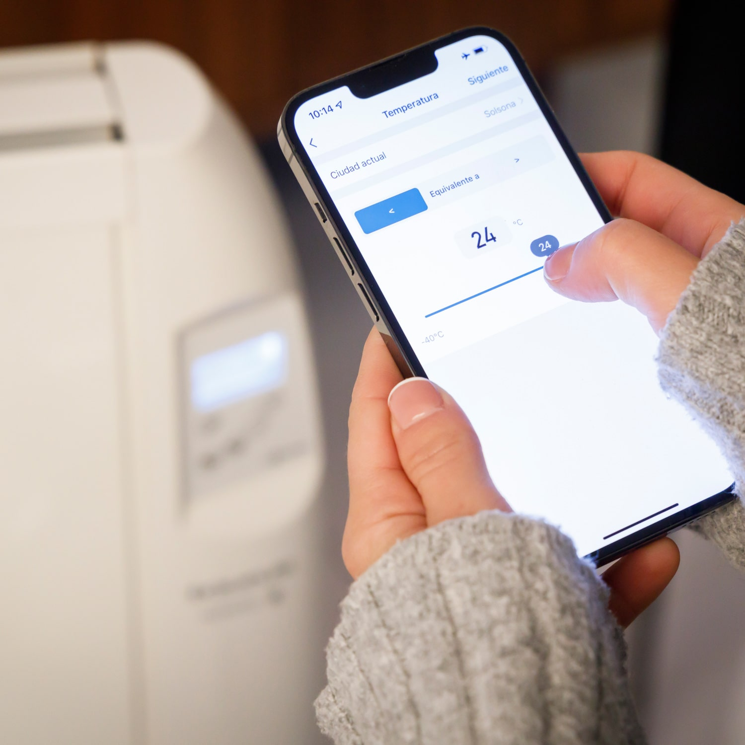Eine Person hält ein Telefon und stellt die Temperatur ein, die auf einem Smart-Home-Gerät angezeigt wird.
