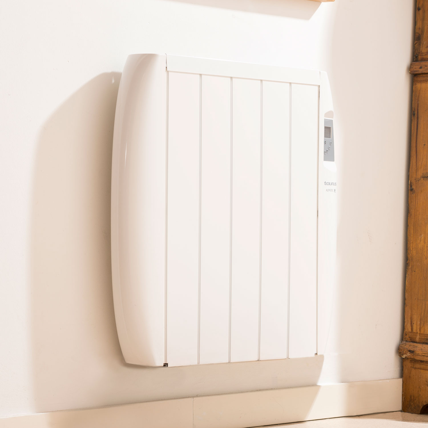 Calentador eléctrico blanco montado en la pared. Pared beige claro y moldura de madera.
