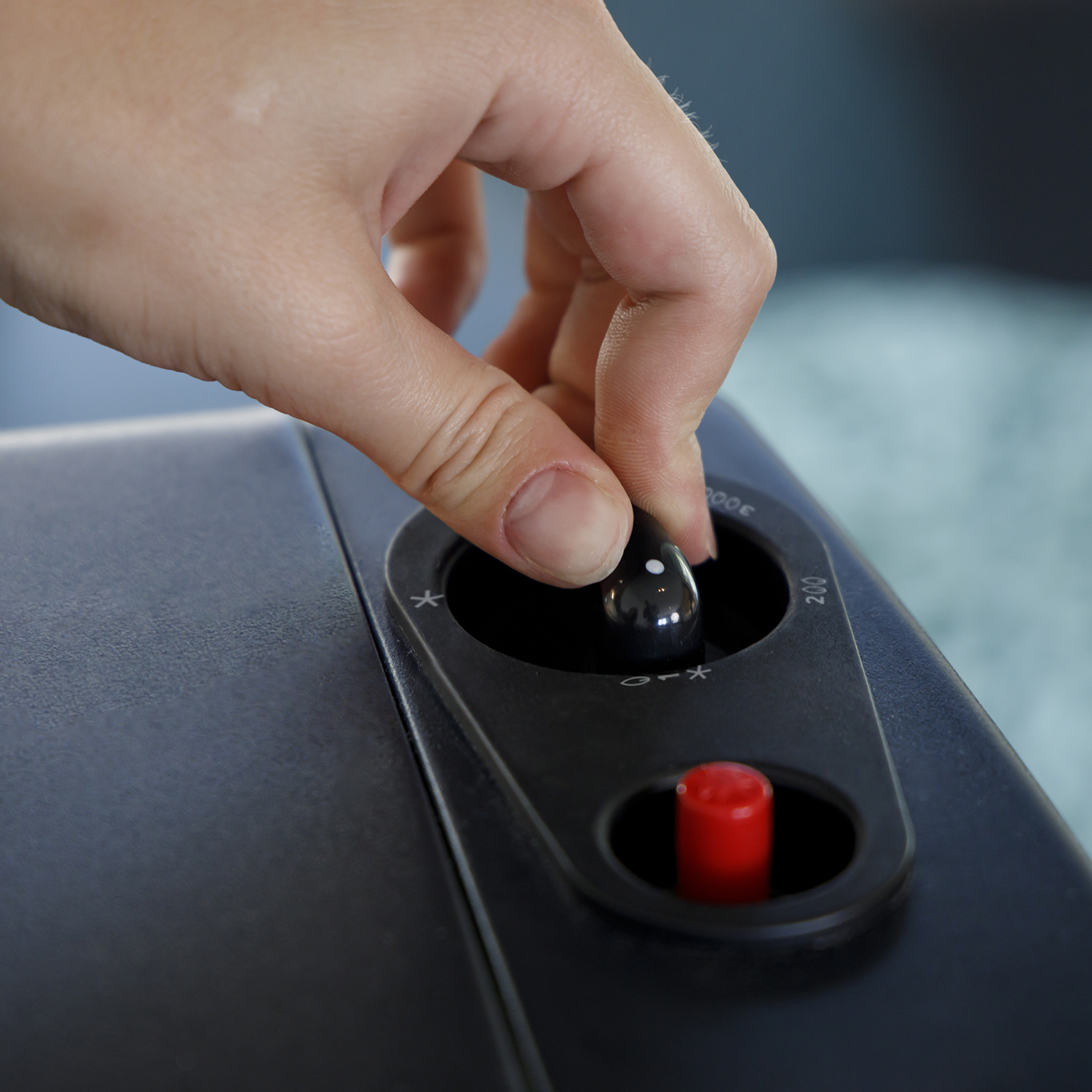 Una mano gira un dial en un dispositivo negro. Un botón rojo está debajo del dial.