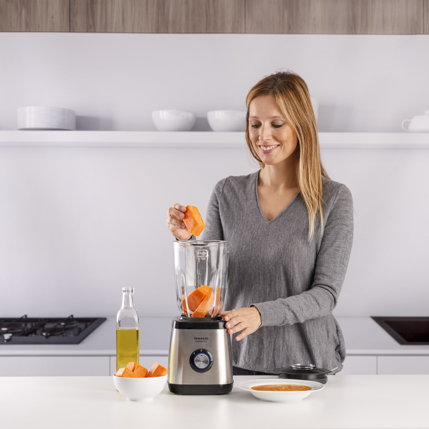 Mujer poniendo trozos de papaya en una licuadora sobre una encimera blanca.