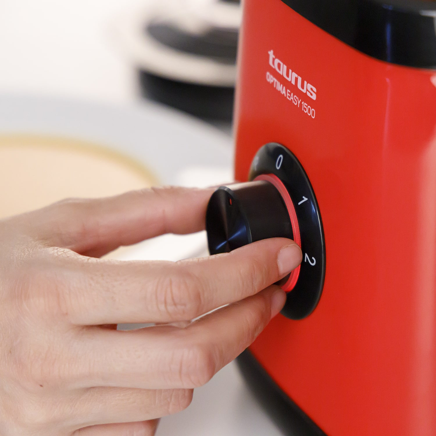Primer plano de una mano girando un dial negro en un electrodoméstico rojo con la marca Taurus.