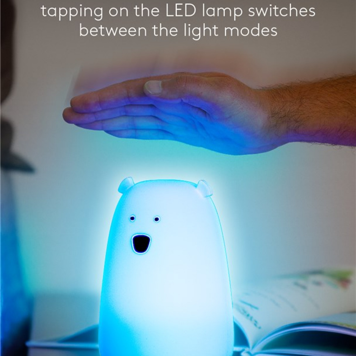 Eine weiße Bärenlampe mit blauem Licht, eine Hand darüber. Text zeigt Tippen schaltet Lichtmodi.