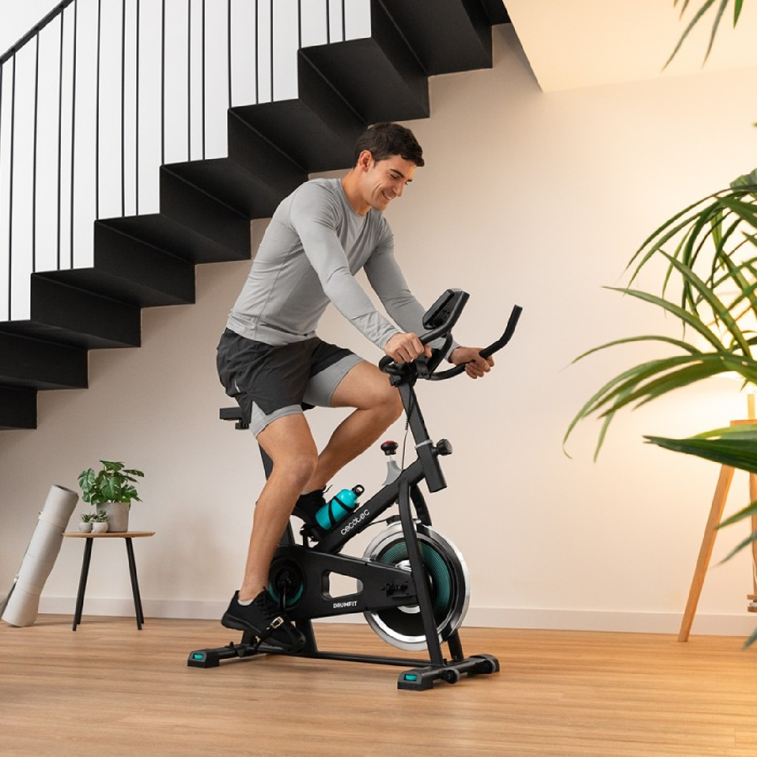 Uomo su cyclette in ambiente domestico. Sorride e si esercita. Arredamento verde e bianco.