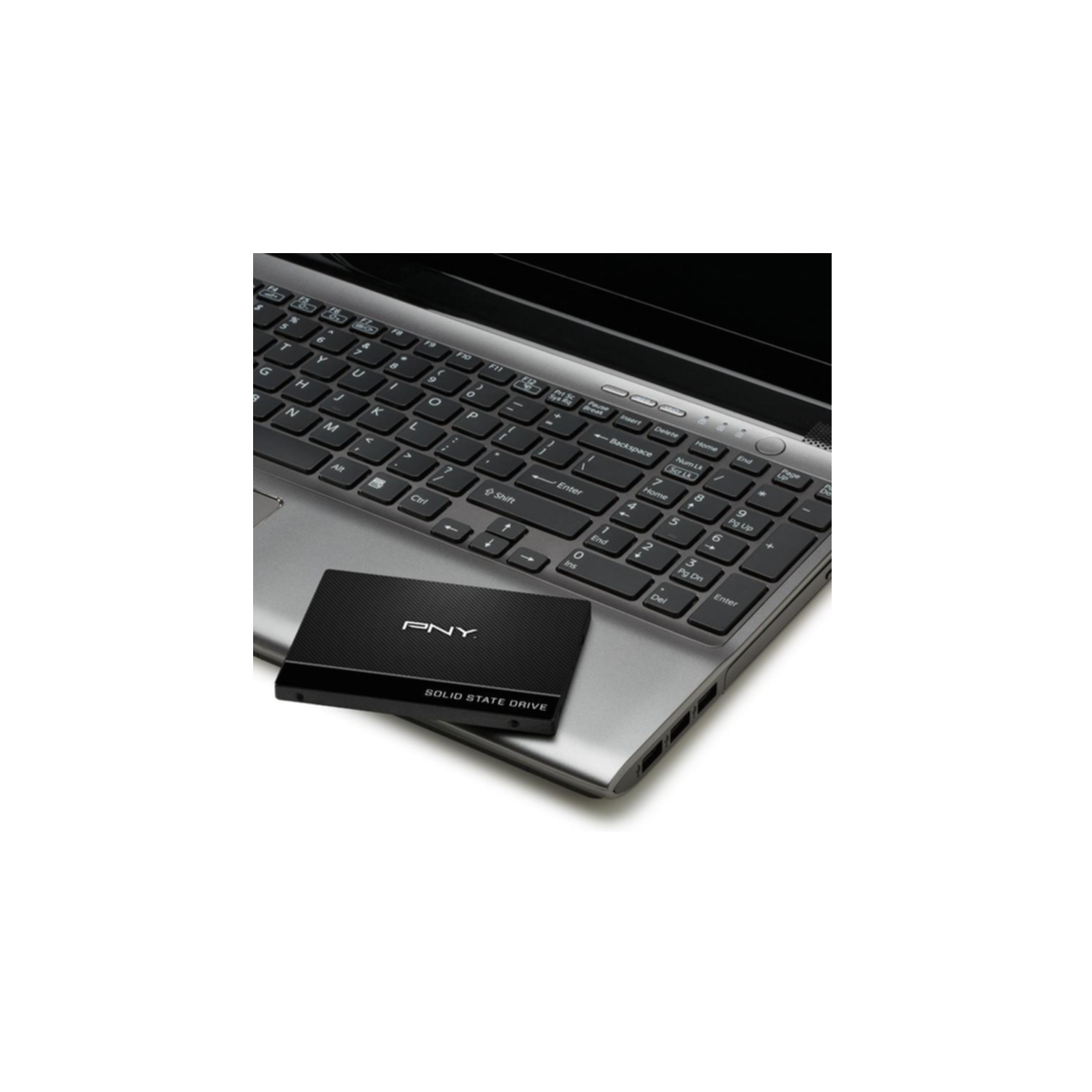 Un SSD nero accanto a un laptop, appoggiato su una scrivania. Tastiera e schermo visibili.