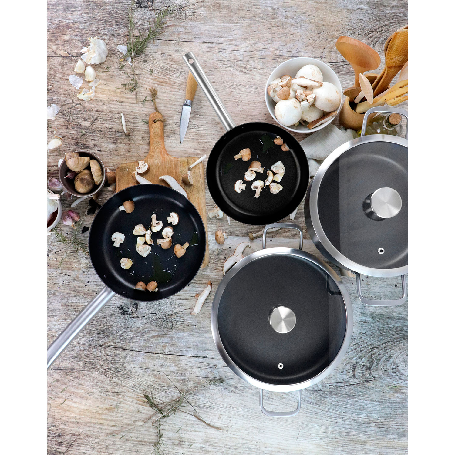 Escena de cocina con sartenes con champiñones y utensilios de cocina sobre una superficie de madera.