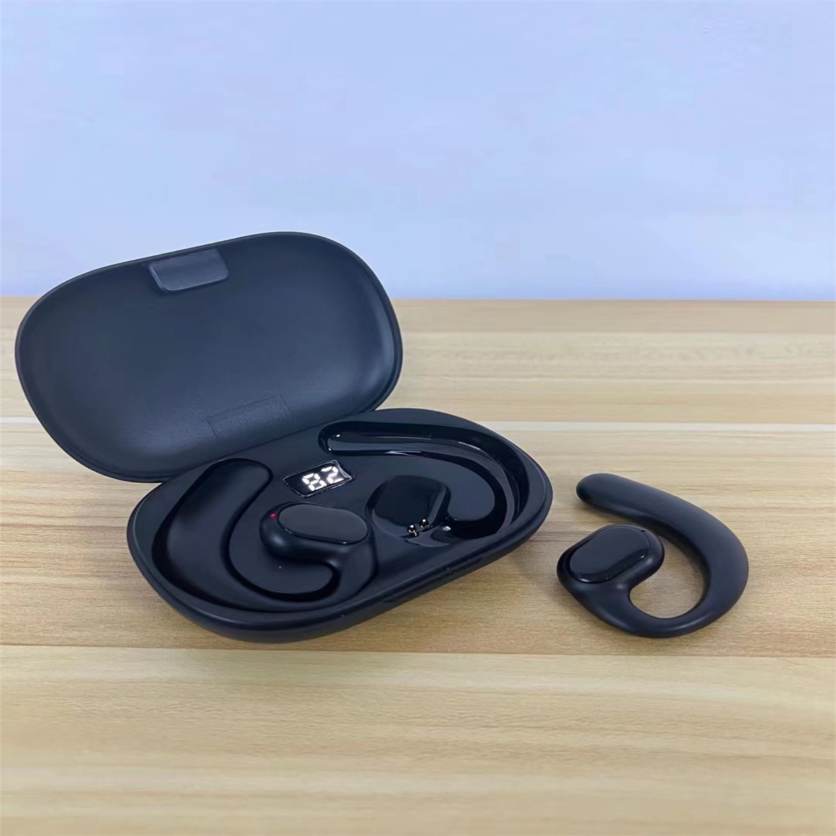Auriculares inalámbricos negros en un estuche de carga negro, con un solo auricular a un lado.