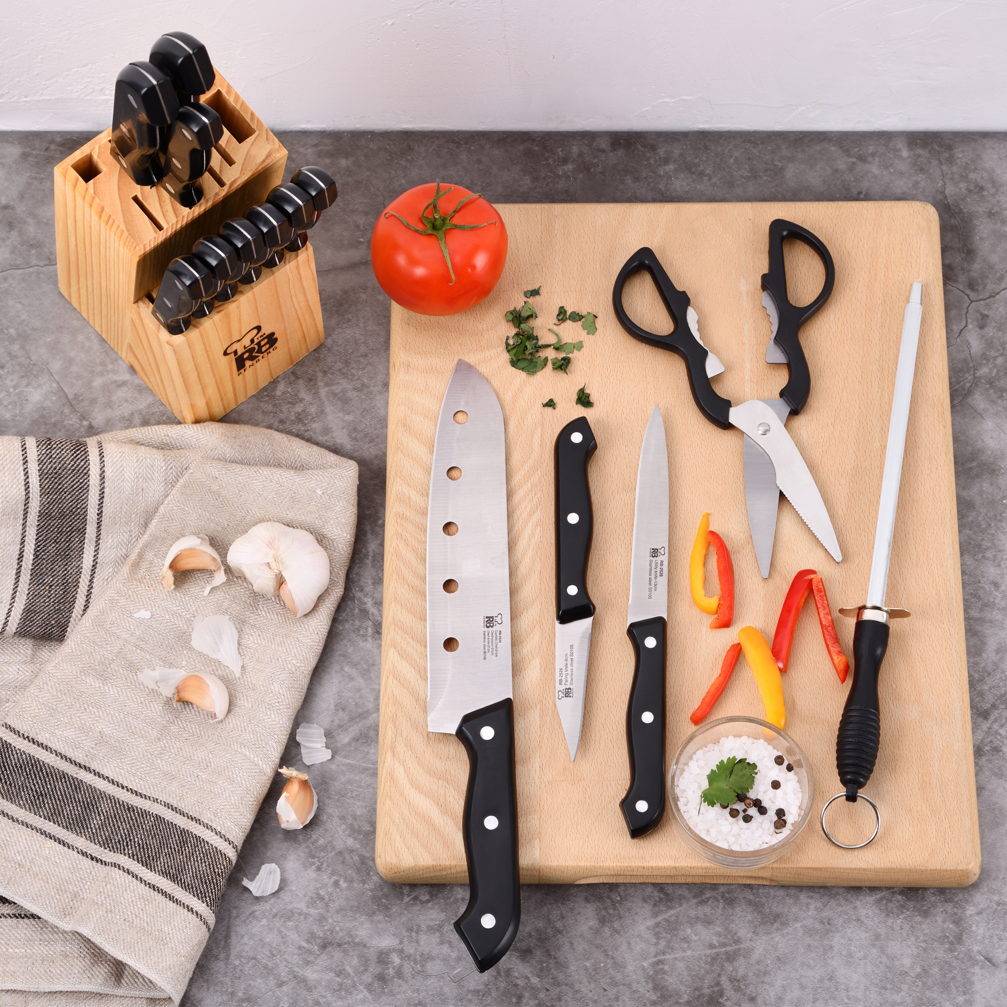 Una escena de cocina con un bloque de cuchillos, cuchillos, tijeras, un tomate y verduras cortadas en una tabla de madera.