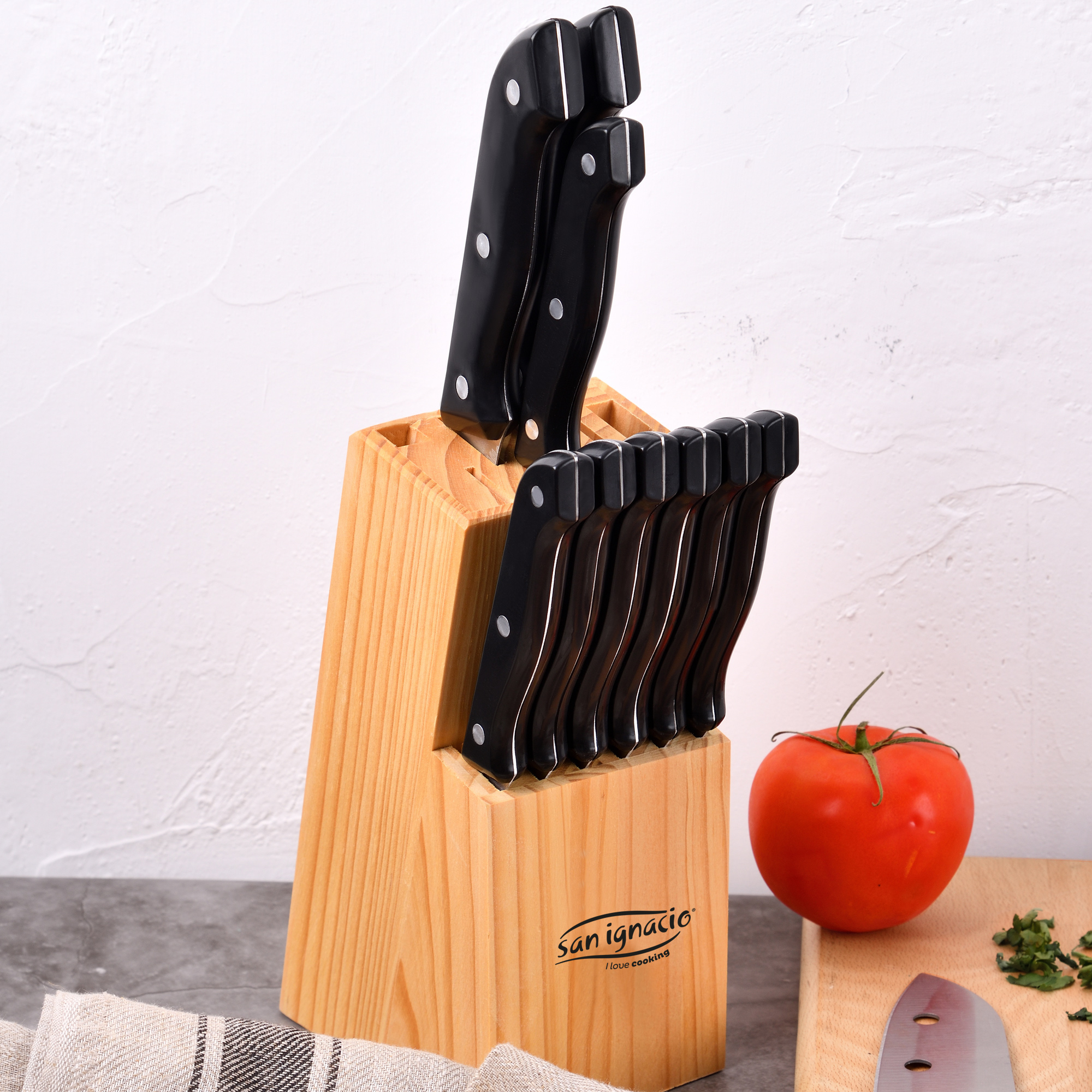 Un bloque de cuchillos de madera con varios cuchillos con mango negro y un tomate rojo.