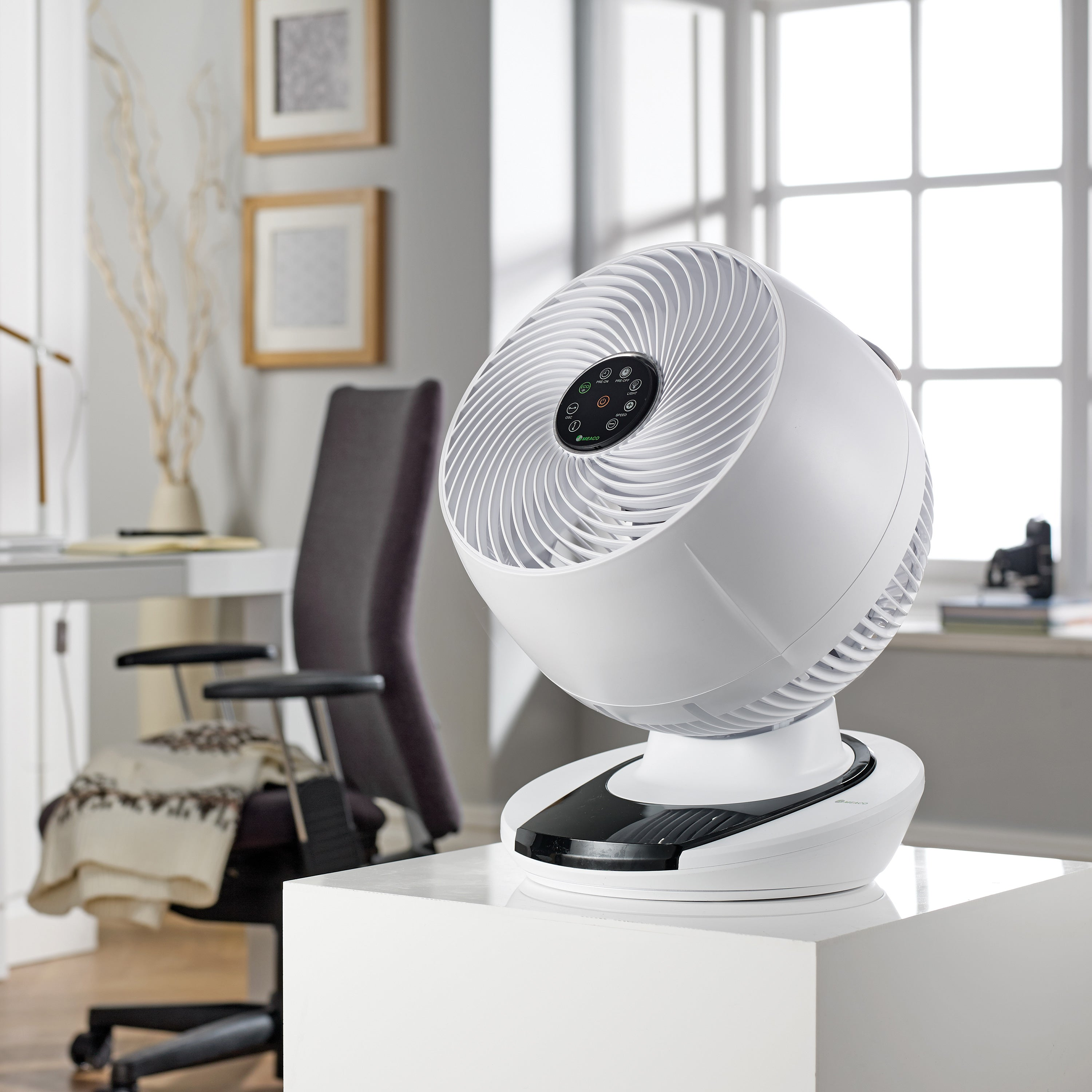 Biały wentylator na białym cokole. Wentylator znajduje się w jasnym pokoju z oknem.