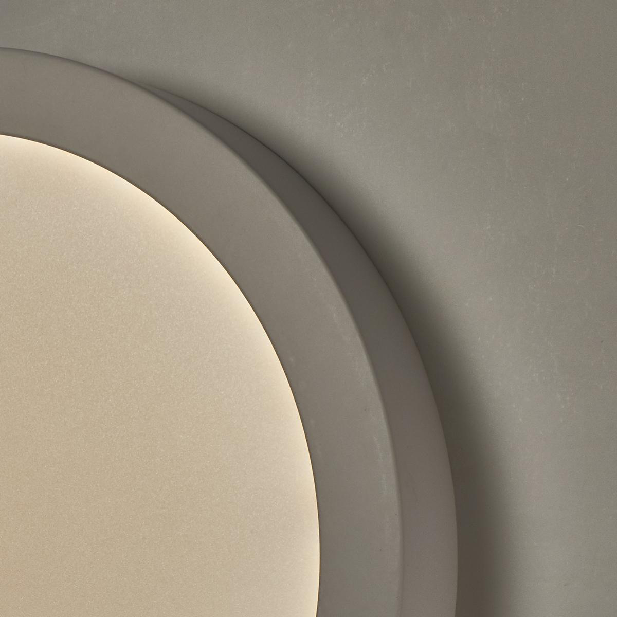 Lampada da soffitto circolare grigia. Il bordo è spesso e curvo. La luce brilla dall'interno.