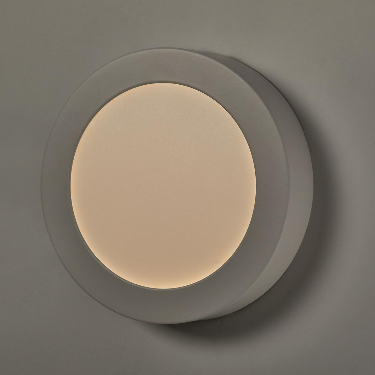 Apparecchio di illuminazione rotondo da soffitto bianco con centro luminoso, su una parete grigia.
