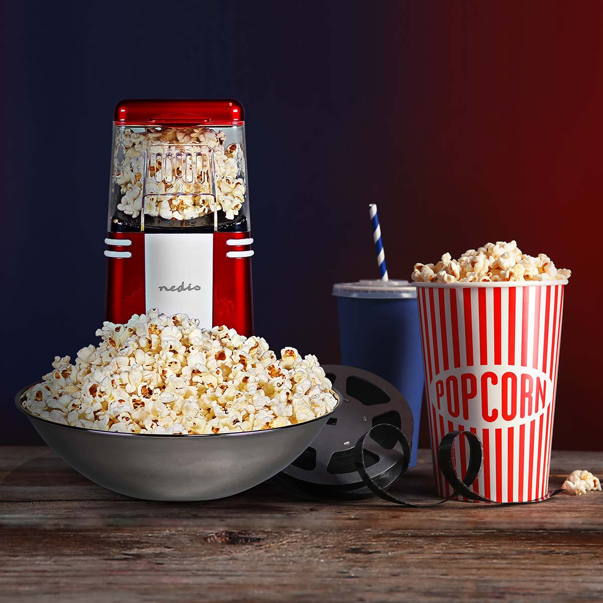 Una macchina per popcorn rossa con popcorn, una ciotola, un bicchiere e un bobina film.