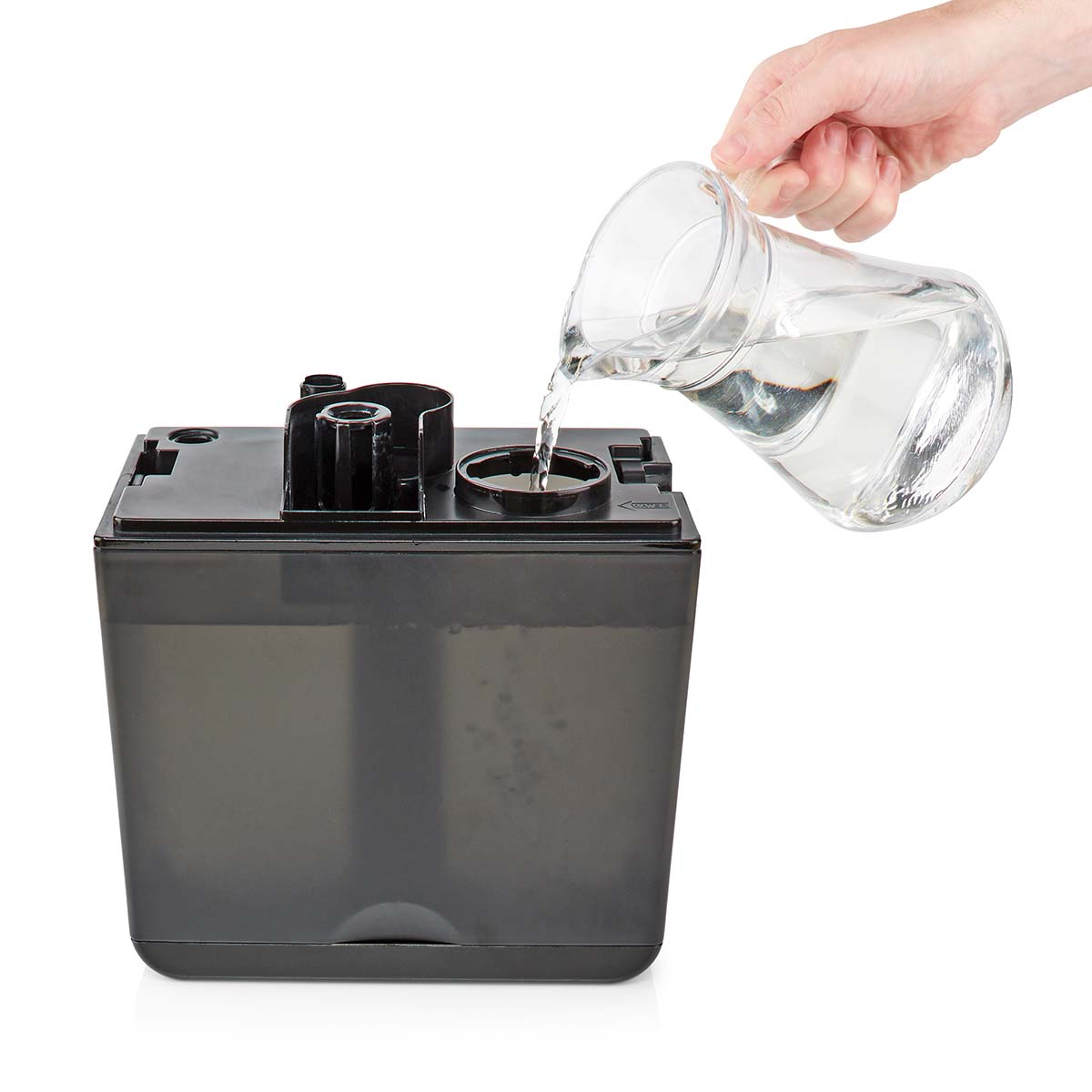 Een hand die water uit een glazen kan in een luchtbevochtiger giet. De luchtbevochtiger is zwart.
