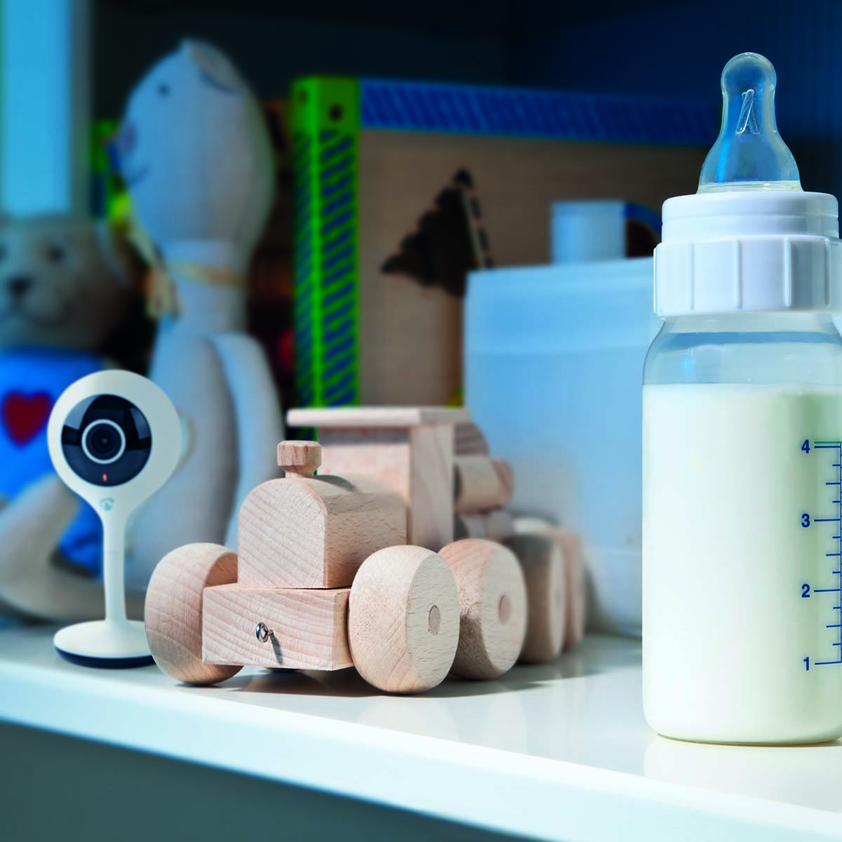 Articoli per bambini su una mensola: fotocamera, camion giocattolo, biberon con latte e un baby monitor.