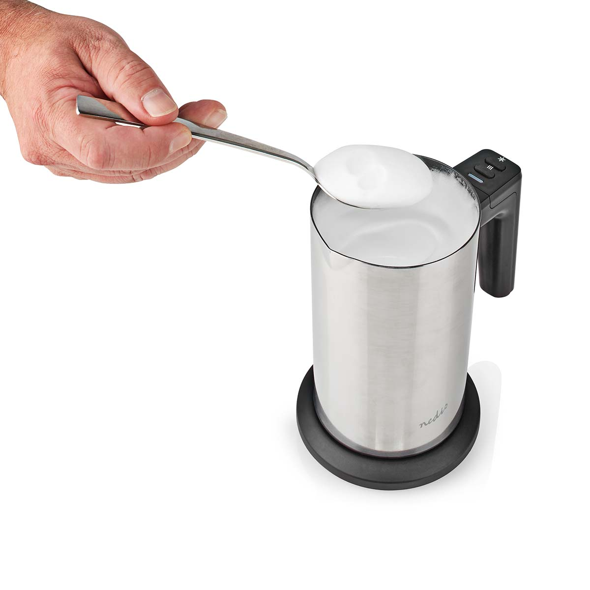 Una mano tiene un cucchiaio con schiuma di latte sopra un montalatte argentato.