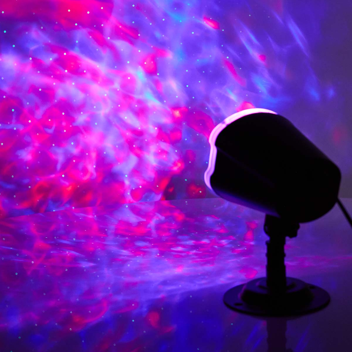 Schwarz-Weiß-Projektor, der rotes und violettes Licht auf eine Wand projiziert. Das Licht hat Sterne.