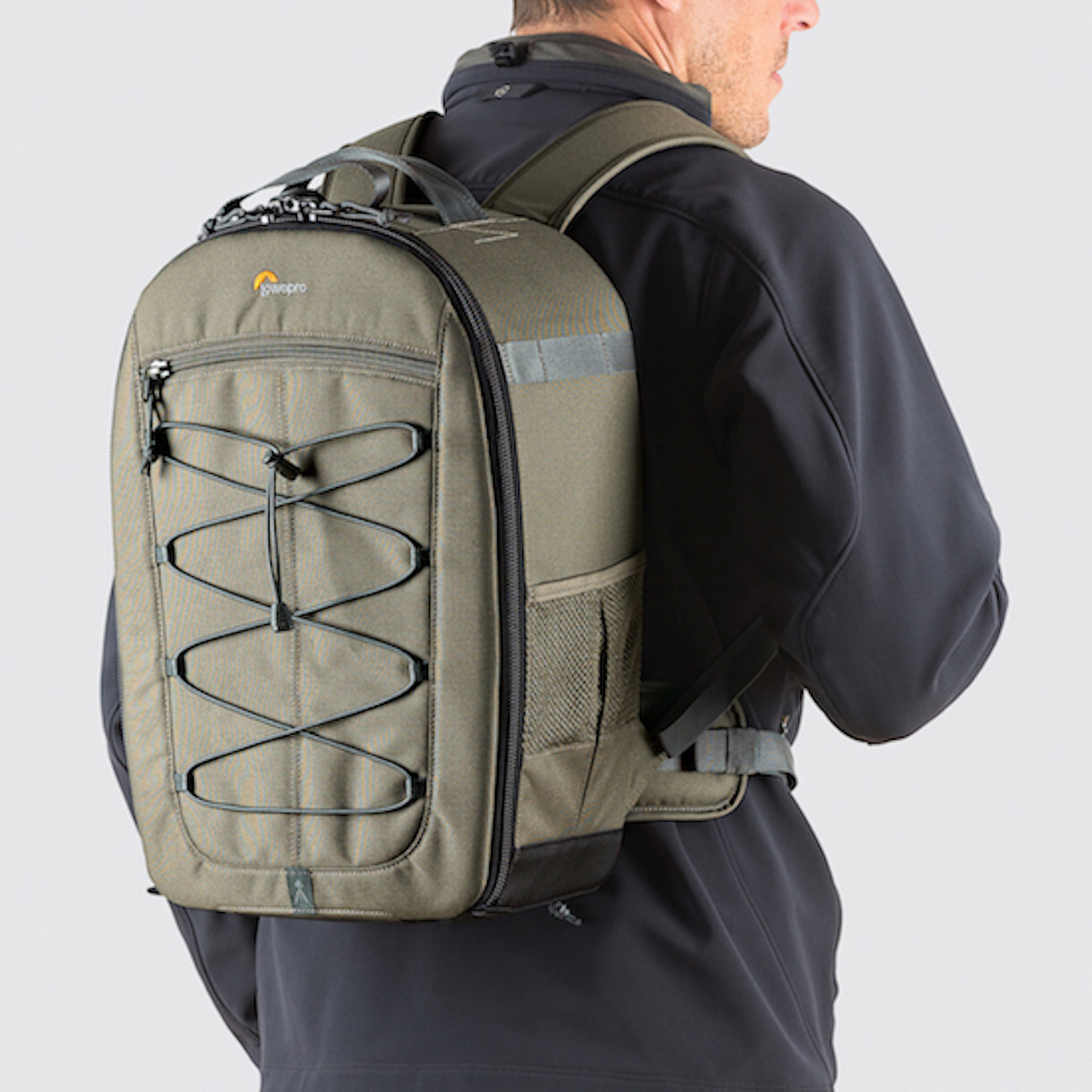 Khaki-Rucksack auf einer Person. Vorne Bungee-Kordeln. Mann in schwarzer Jacke. Weißer Hintergrund.