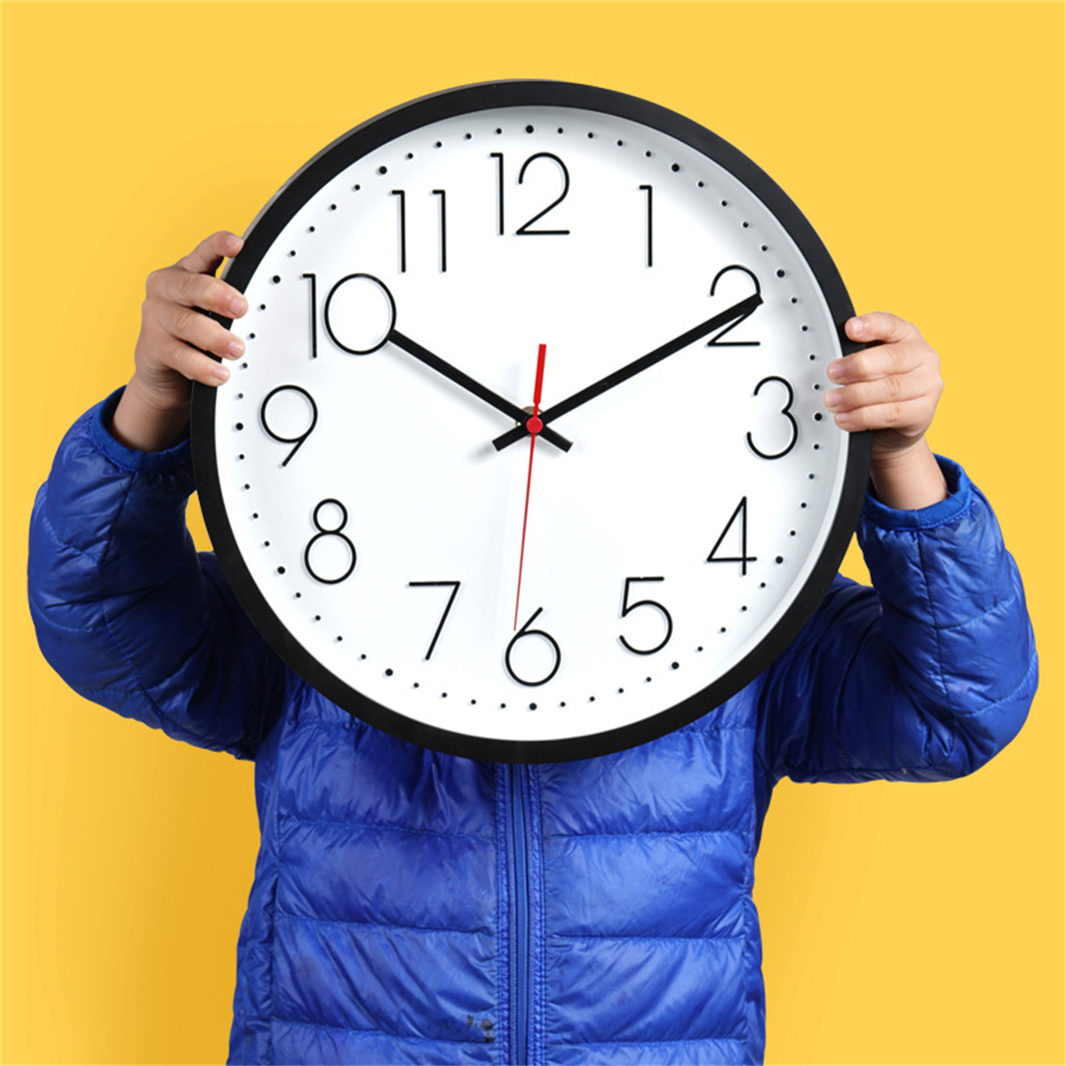 Manos de una persona sosteniendo un reloj grande frente a su cara, con una chaqueta azul.