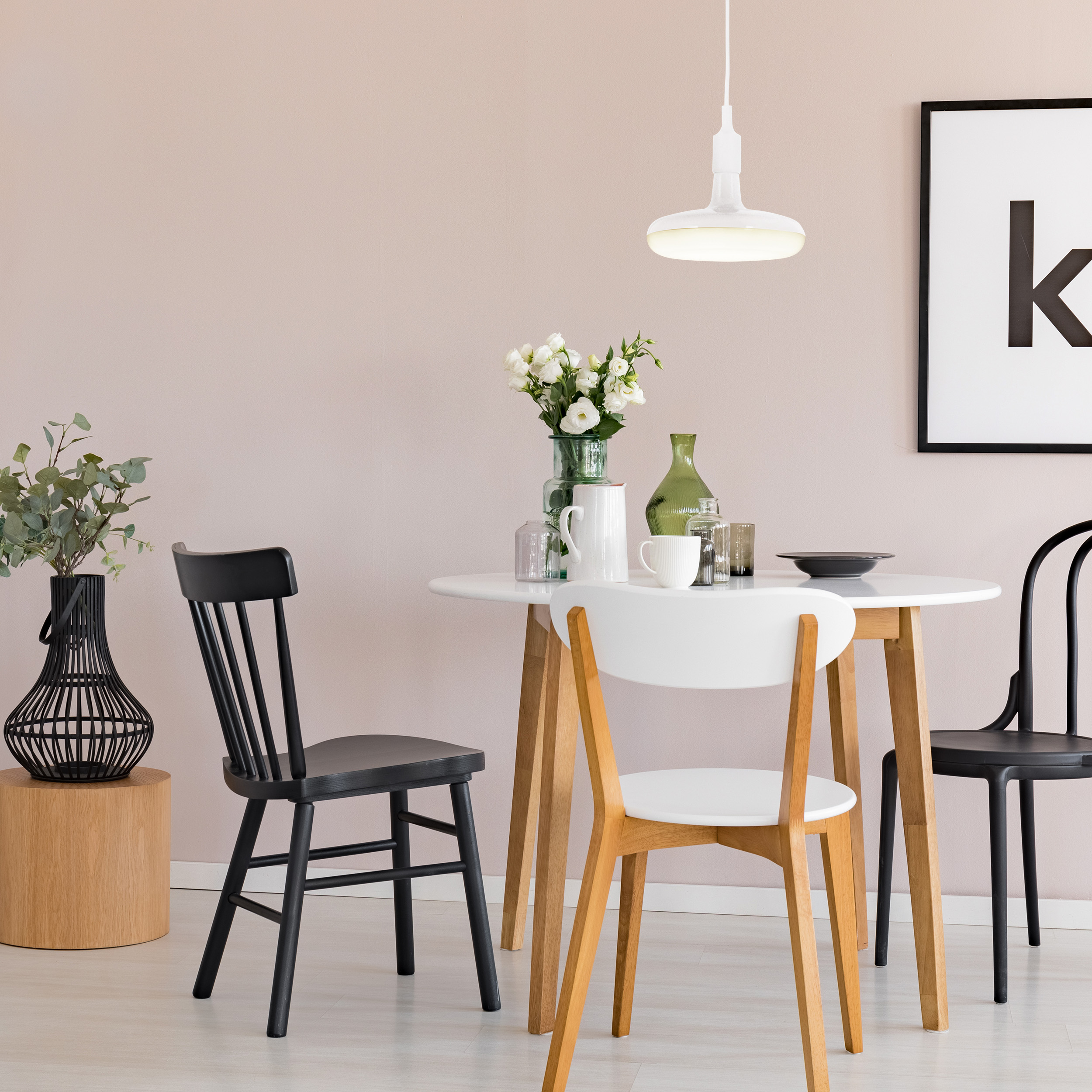 Ein Esszimmer mit rundem Tisch, Stühlen und Dekoration. Schwarz-weiße Stühle und eine Blumenvase.