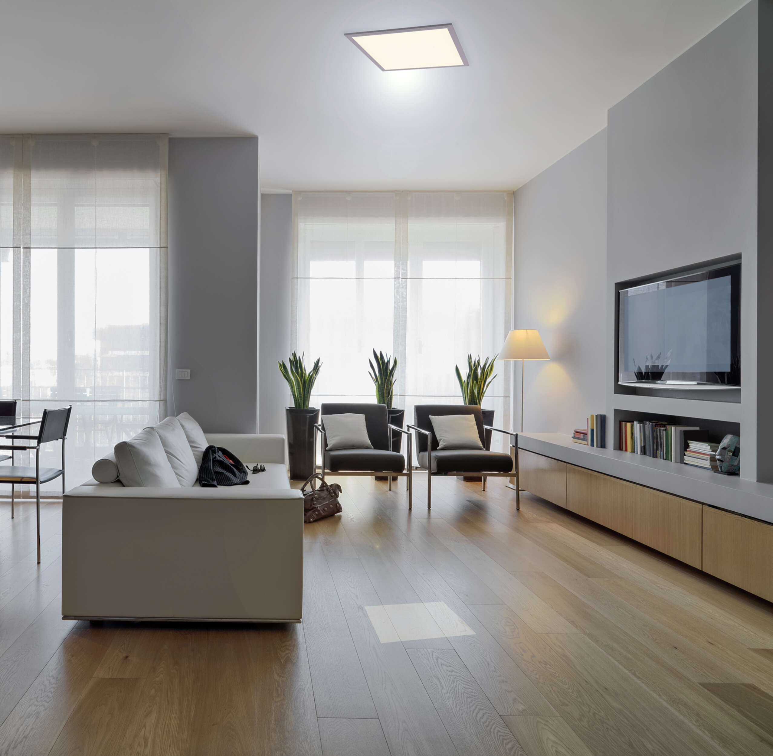 Ein modernes Wohnzimmer mit weißem Sofa, dunklen Stühlen und Holzboden.
