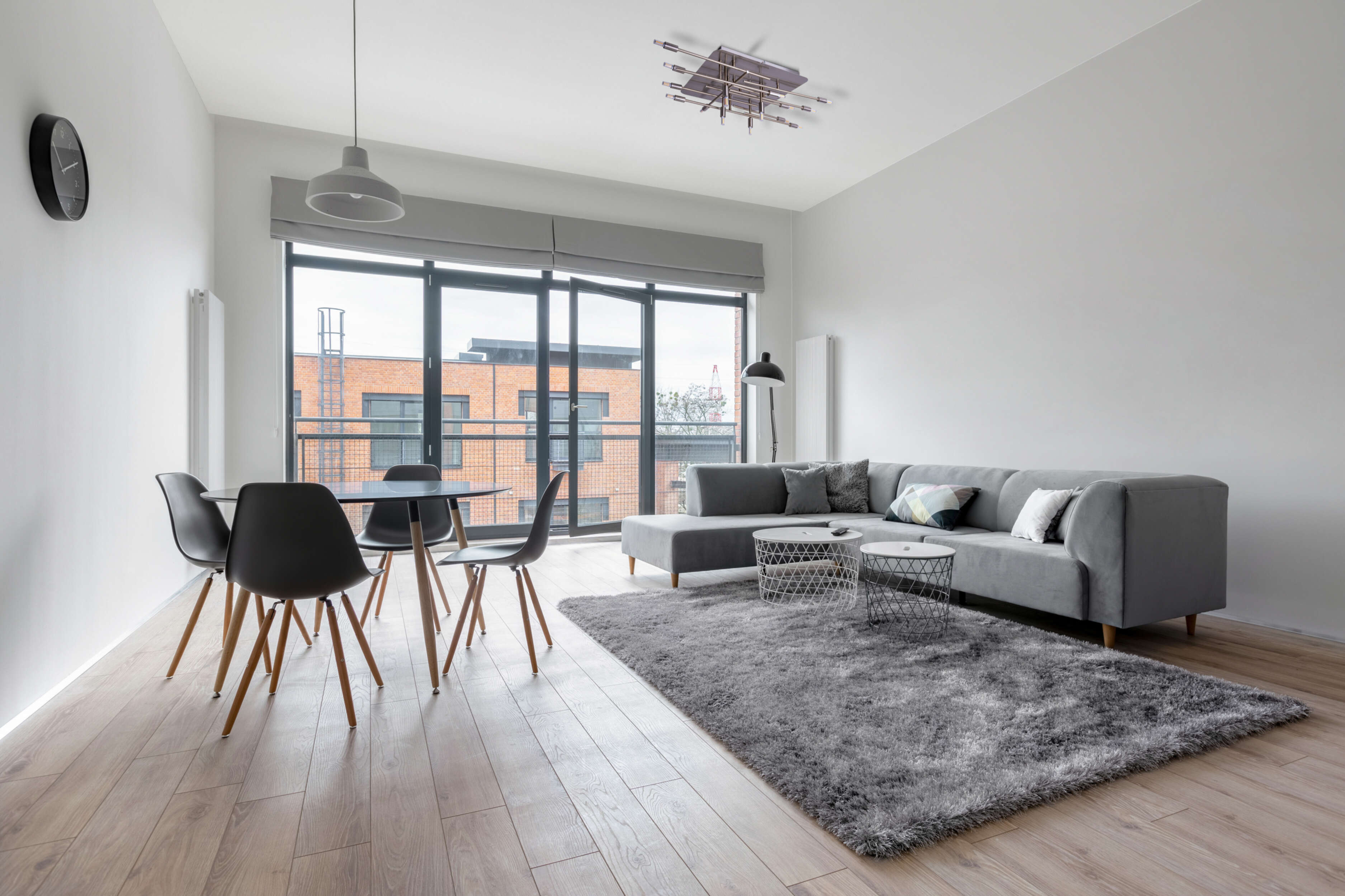 Ein modernes Wohnzimmer mit grauem Sofa, Esstisch und großem Fenster.