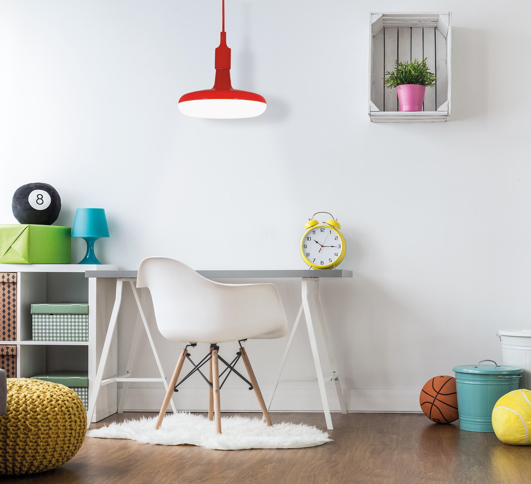 Ein helles Kinderzimmer mit einer roten Pendelleuchte, einem Schreibtisch und einem weißen Stuhl. Buntes Spielzeug und Deko.
