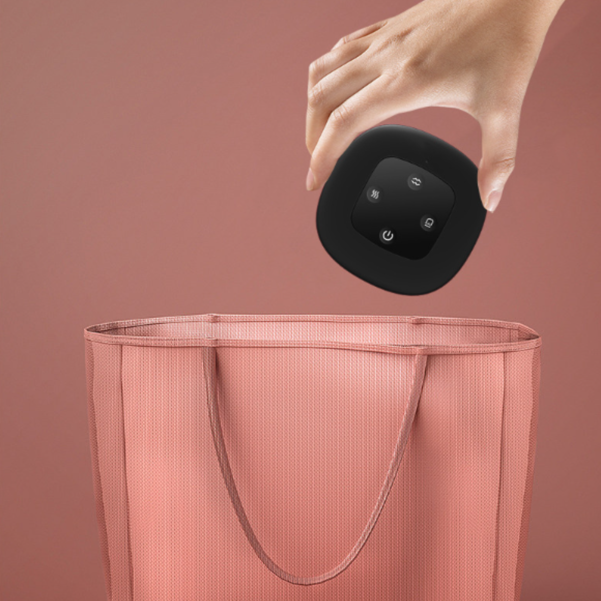 Una mano colocando un dispositivo negro en una bolsa rosa. Fondo rosa.