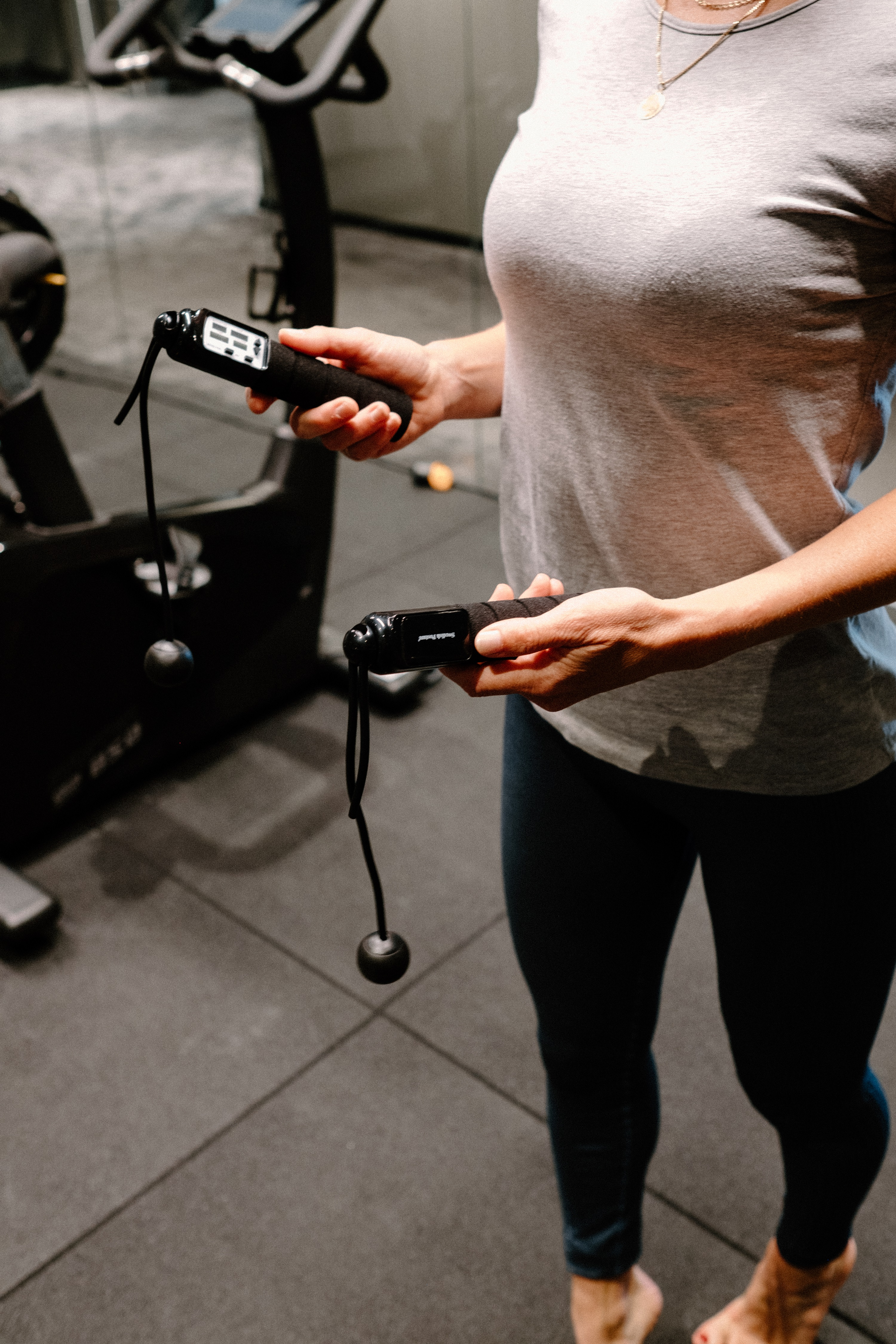Eine Frau hält zwei schwarze Springseile in einem Fitnessstudio.