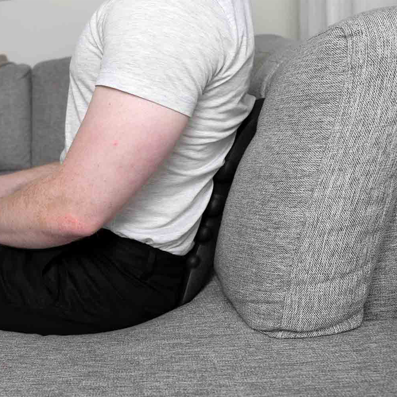 Mann sitzt auf grauem Sofa mit Rückenstütze. Schwarzes Kissen.