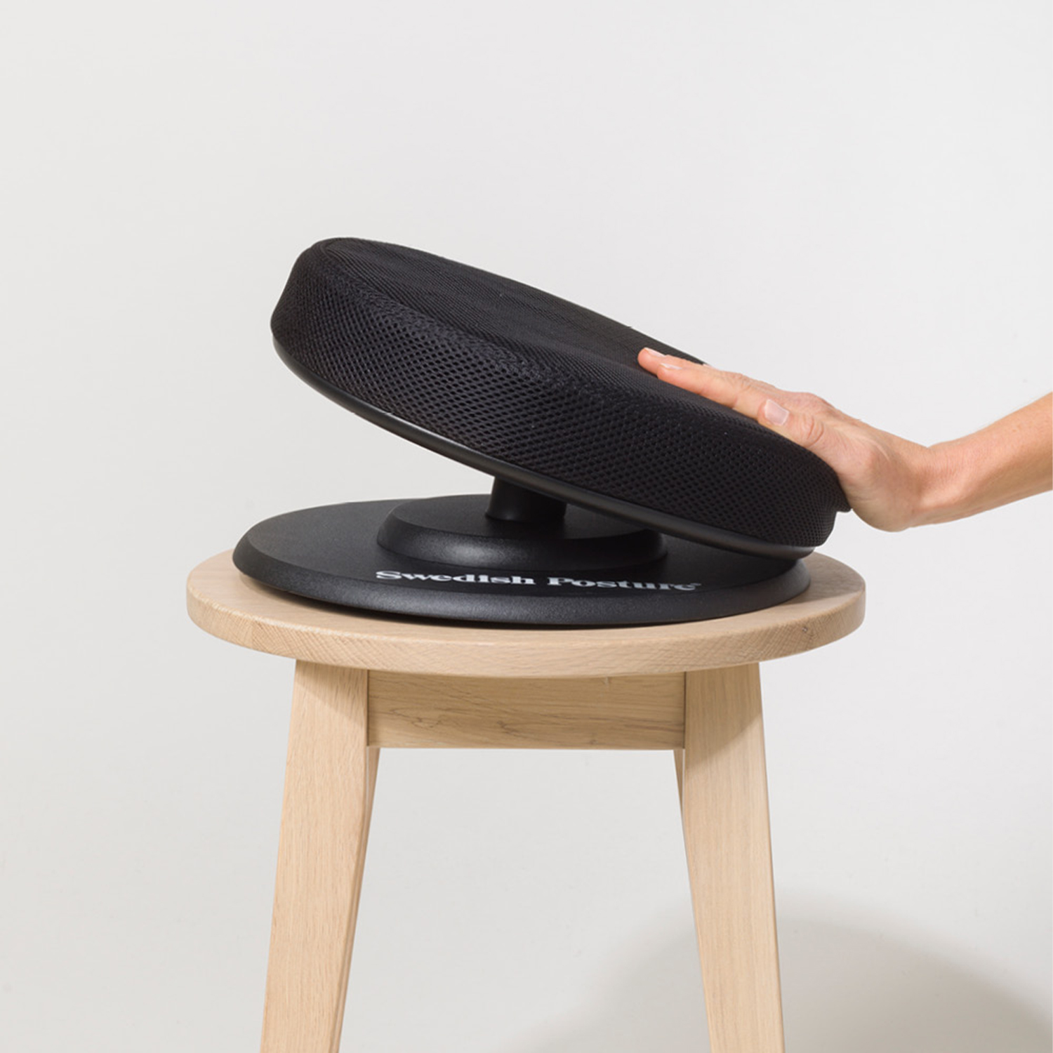 Hand einer Person, die einen schwarzen Sitz auf einem Hocker einstellt. Weißer Hintergrund.