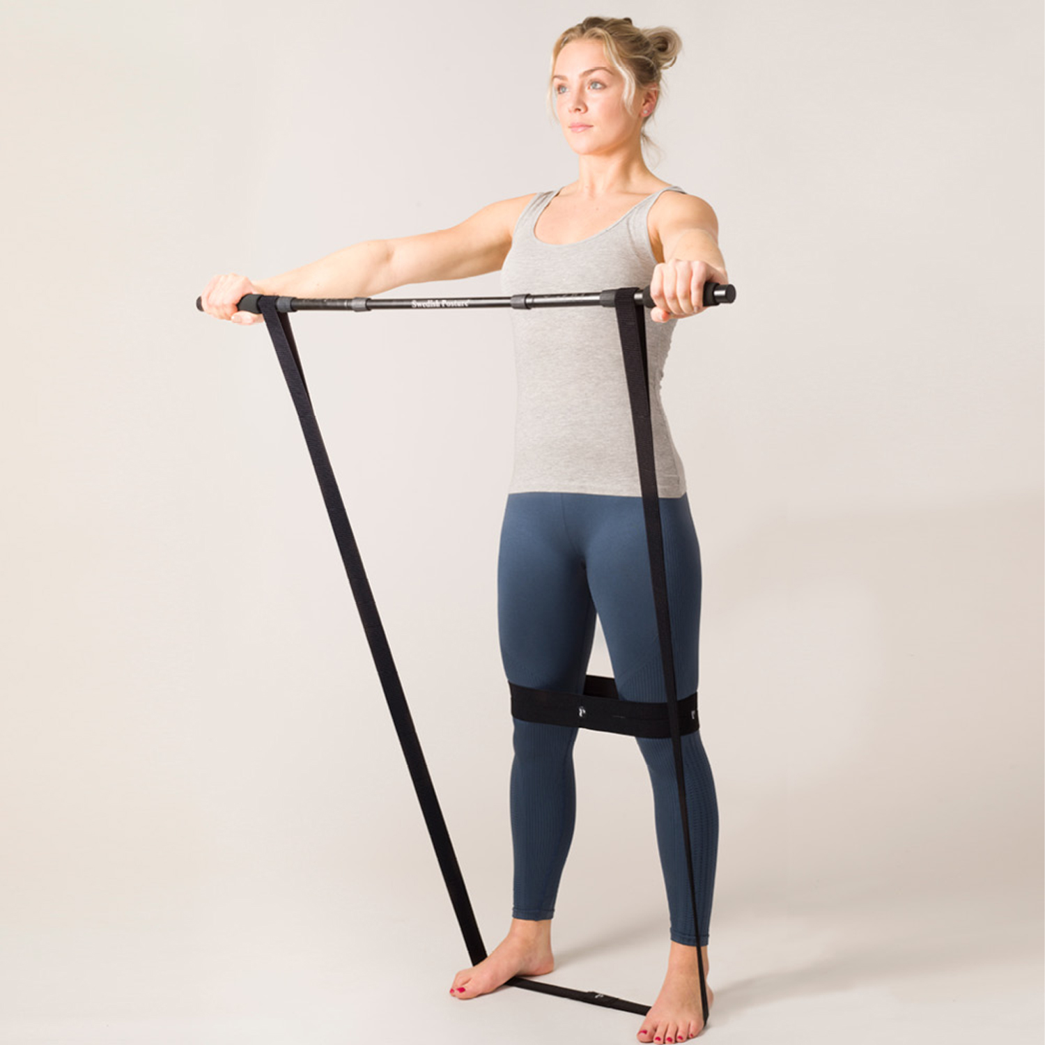 Frau in grauem Tanktop und Leggings, die einen Fitness-Barren mit schwarzen Bändern benutzt.