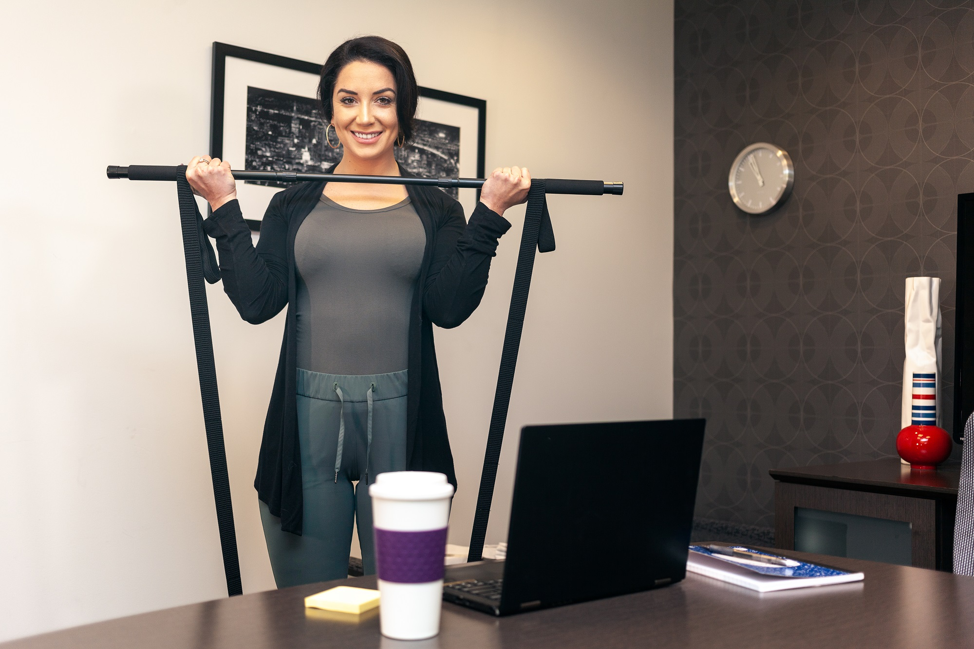 Frau im Büro, die eine Stange hält, Laptop und Kaffeetasse auf dem Schreibtisch.